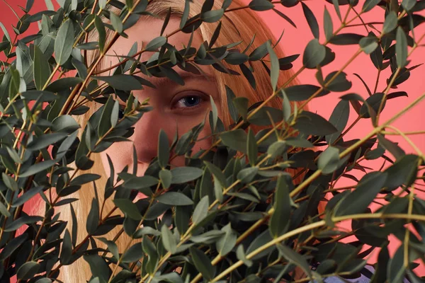 Close-up shot of young woman hiding behind bunch of eucalyptus branches — Stock Photo