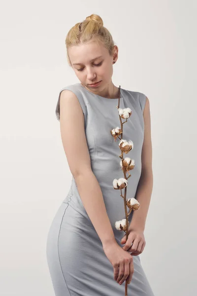 Attractive young woman in grey dress with cotton branch isolated on white — Stock Photo