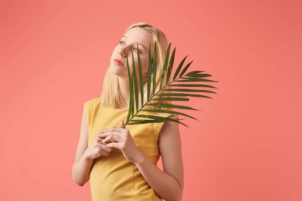 Jeune femme réfléchie avec branche de palmier isolé sur rouge — Photo de stock