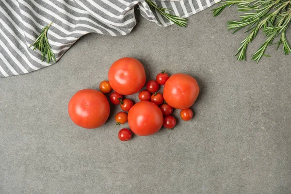 Top view of ripe fresh tomatoes on grey concrete surface with linen and rosemary — Stock Photo