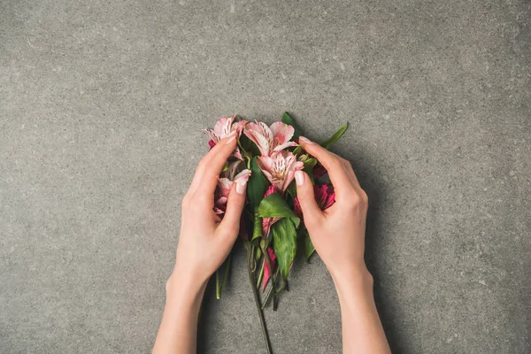 Teilansicht weiblicher Hände und schöner peruanischer Lilien auf grauer Betontischplatte — Stockfoto