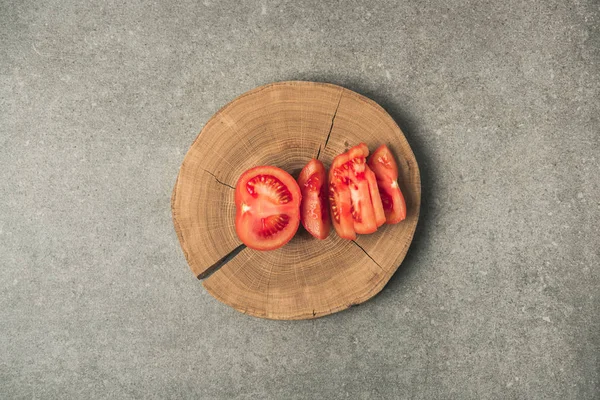 Vista superior del tomate cortado sobre un tocón de madera sobre una mesa de hormigón gris - foto de stock