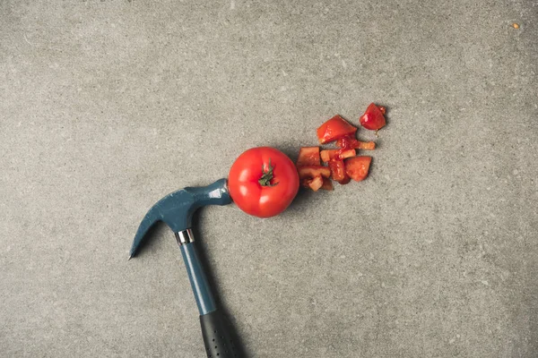 Flat lay with cut fresh tomato, tomato pieces and hammer on grey concrete teblatop — Stock Photo