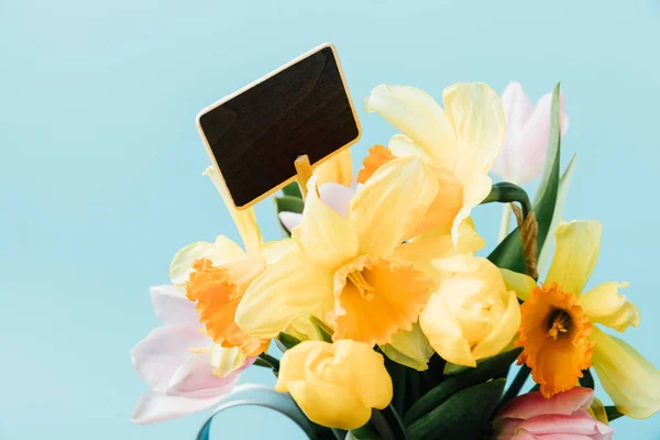 Закрытый вид на красивые тюльпаны, цветы нарцисса и черную доску, изолированную на голубом фоне — стоковое фото