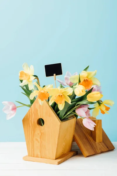 Close up view of beautiful bouquet of flowers with blank chalkboard in birdhouse on wooden tabletop isolated on blue — Stock Photo