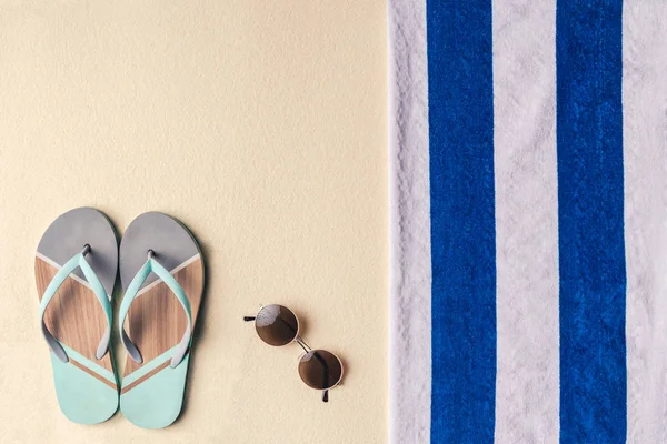 Flip flops and sunglasses by towel on sandy beach — Stock Photo