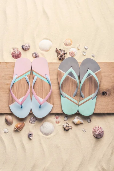 Flip flops and seashells on wooden pier on light sand — Stock Photo