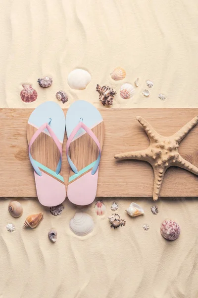 Flip flops and starfish with shells on light sand — Stock Photo