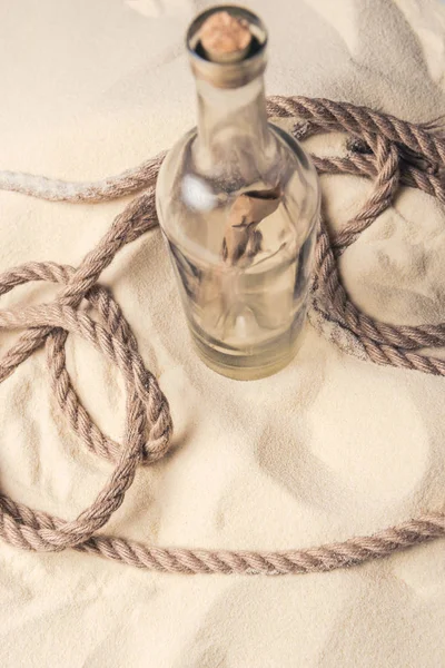 Bottle with letter and rope on light sand — Stock Photo