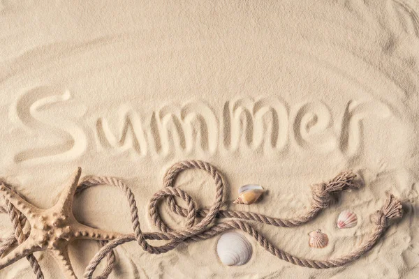 Estrella de mar y conchas con cuerda sobre arena clara con inscripción de verano - foto de stock