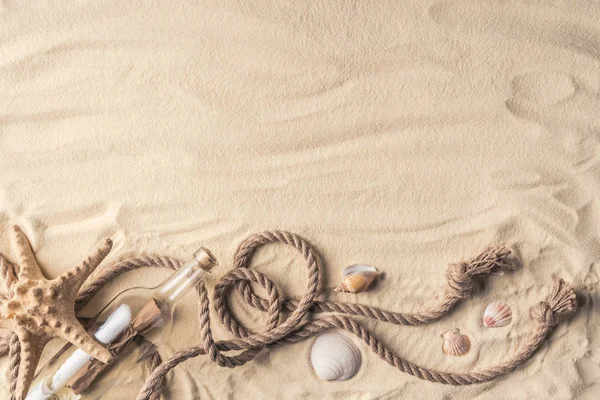 Bottle with letter and shells with rope on light sand — Stock Photo