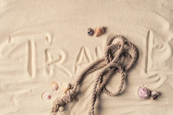 Corde et coquilles sur la plage de sable avec corde et inscription Voyage — Photo de stock