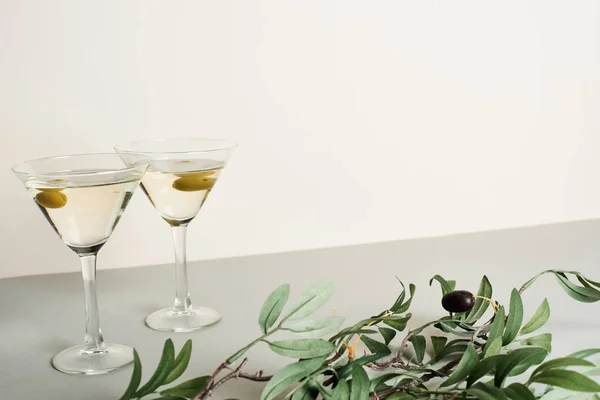Two glasses with cocktails and olive branch on grey surface isolated on white — Stock Photo
