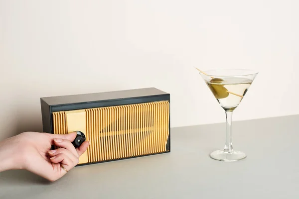 Vista cortada da mulher ajustando o volume de rádio retro com coquetel martini ao lado — Fotografia de Stock