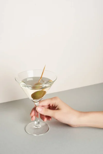 Cropped view of woman holding martini cocktail on grey surface on white background — Stock Photo