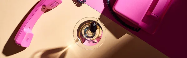 Vista superior de martini en vidrio con teléfono rosa sobre fondo colorido, plano panorámico - foto de stock