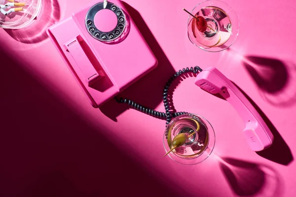 Top view of cocktails and telephone handset beside astray with cigarette butts on pink surface — Stock Photo