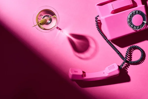 Вид сверху на стекло с мартини и ретро-телефоном на розовом фоне — стоковое фото