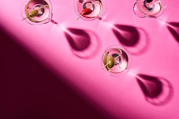 Вид сверху на коктейли мартини с оливками на розовом фоне — стоковое фото