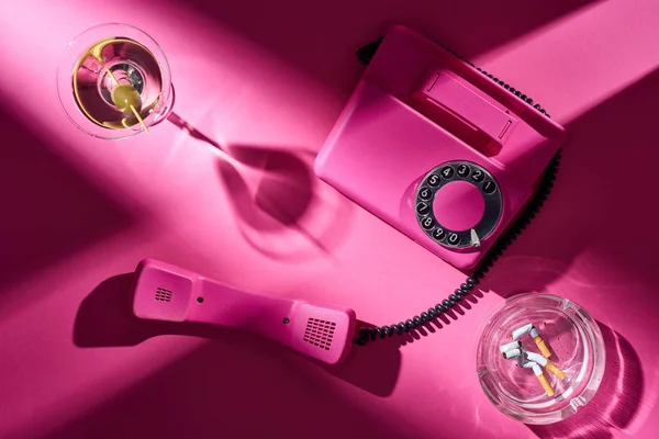 Top view of pink telephone, cocktail and astray with cigarette butts on pink surface — Stock Photo