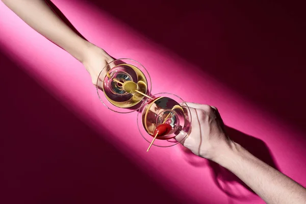 Cropped view of man and woman holding cocktails on pink background with shadow — Stock Photo