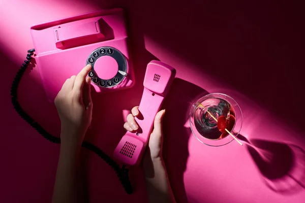 Cropped view of woman using retro telephone with martini beside on pink background — Stock Photo