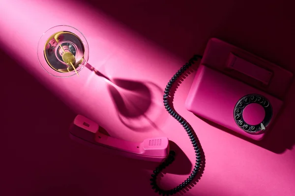 Вид сверху на мартини и ретро телефон на ярко-розовом фоне — стоковое фото