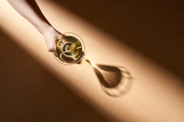 Cropped view of woman holding glass of martini on beige background — Stock Photo