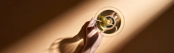 Vista recortada de la mujer sosteniendo en vaso de mano de martini sobre fondo beige, plano panorámico - foto de stock