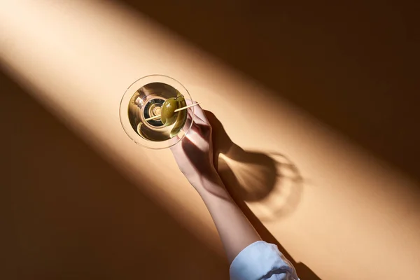 Vista recortada de la mujer sosteniendo martini sobre fondo beige con sombra - foto de stock