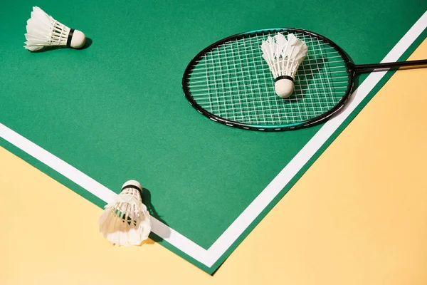 Vista de ángulo alto de raqueta de bádminton y lanzaderas en pista verde sobre superficie amarilla - foto de stock