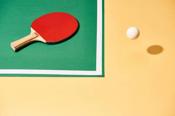 Vista en ángulo alto de la raqueta de tenis en la mesa y la bola en la superficie amarilla - foto de stock