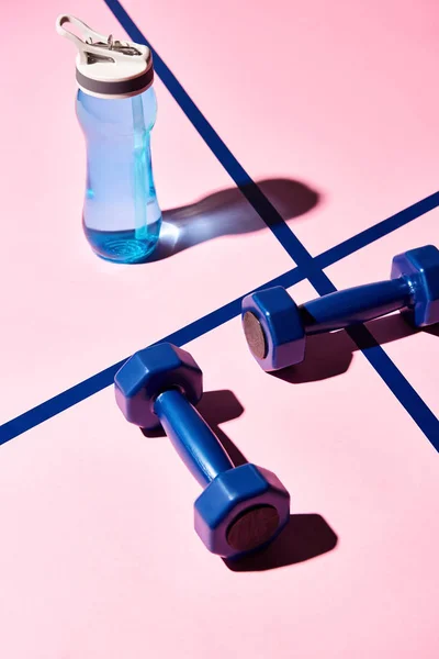 High angle view of dumbbells and water bottle on pink background — Stock Photo