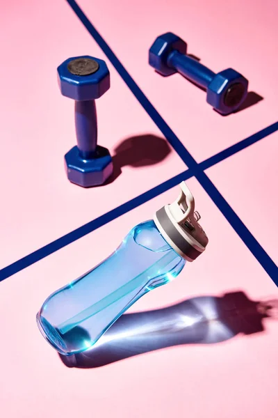 Sport-Wasserflasche mit Hanteln im Hintergrund auf rosa Oberfläche — Stockfoto