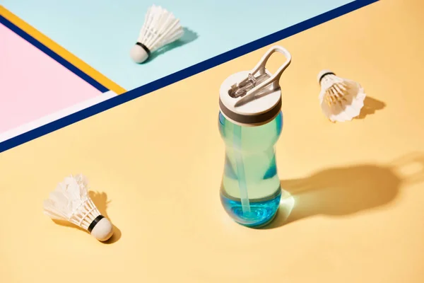 Бутылка воды и шаттлы бадминтона на поверхности с красочными линиями — стоковое фото
