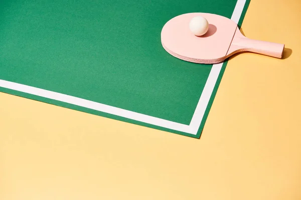 Balle de ping-pong sur raquette et table verte sur surface jaune — Photo de stock