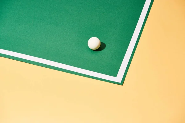 Pelota de tenis de mesa con sombra sobre fondo verde y amarillo - foto de stock