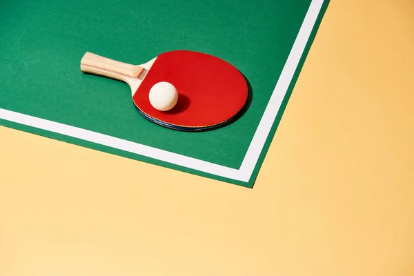 Raqueta de madera y pelota de ping pong en superficie verde y amarilla - foto de stock