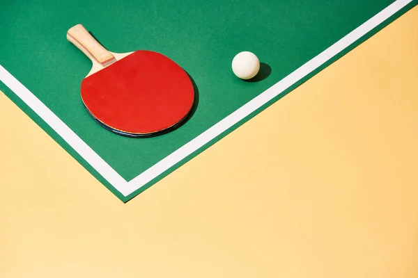 Raquete de tênis de mesa e bola na superfície verde e amarela com linha branca — Fotografia de Stock