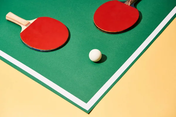 Червоні настільні тенісні ракетки та м'яч на зеленій та жовтій поверхні — стокове фото