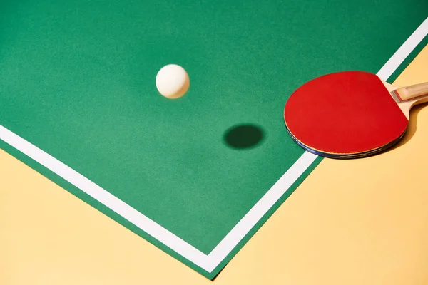 Червоний настільний теніс ракетка і м'яч на платному столі і жовтій поверхні — Stock Photo
