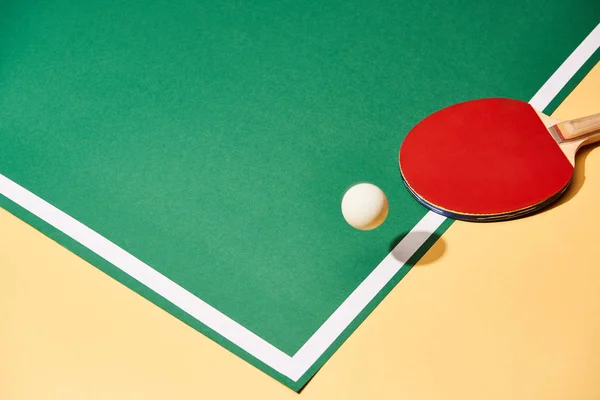 Ball and ping pong racket on yellow and green surface — Stock Photo