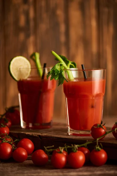 Enfoque selectivo de cóctel María sangrienta en vasos con lima y apio sobre fondo de madera con tomates — Stock Photo