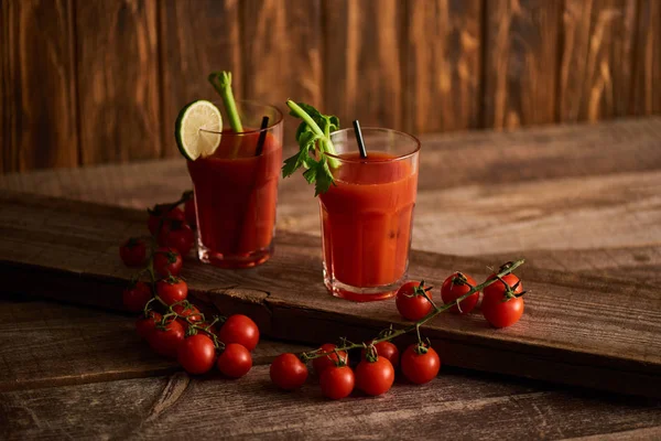 Bloody mary cocktail in glasses with lime and celery on wooden background with tomatoes — Stock Photo