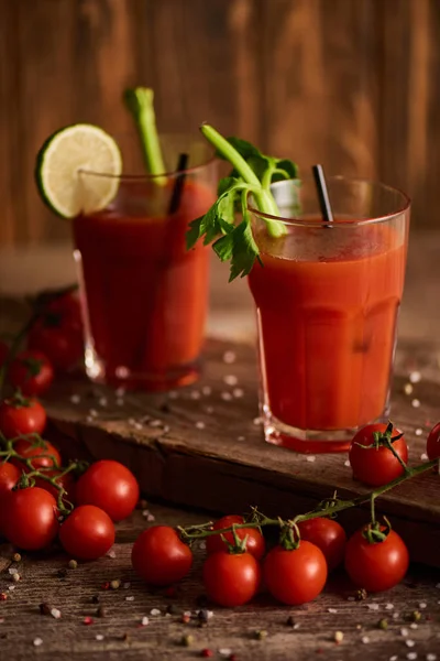 Selective focus of bloody mary cocktail in glasses on wooden background with salt, pepper, tomatoes and celery — Stock Photo