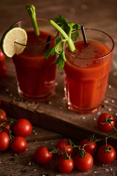 Bloody mary cocktail in glasses on wooden background with salt, pepper, tomatoes and celery — Stock Photo