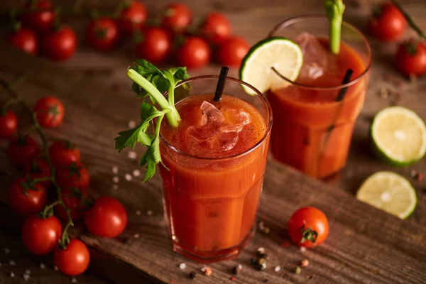 Selective focus of bloody mary cocktail in glasses on wooden background with salt, pepper, tomatoes and celery — Stock Photo