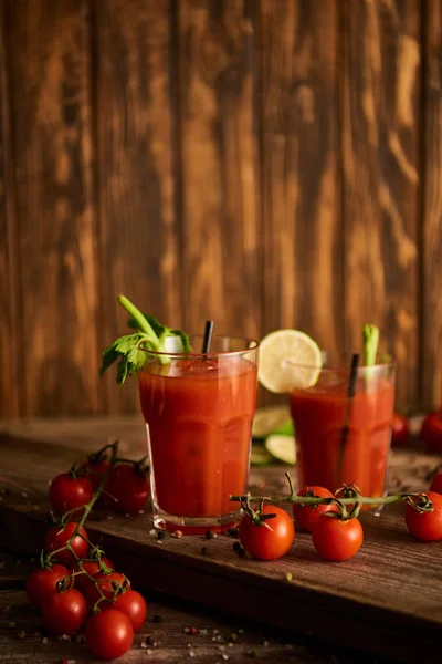 Selektiver Fokus des blutigen Cocktails in Gläsern auf hölzernem Hintergrund mit Salz, Pfeffer, Tomaten und Sellerie — Stockfoto