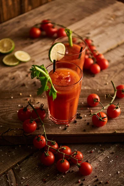Enfoque selectivo de cóctel María sangrienta en vasos sobre fondo de madera con sal, pimienta, tomates y apio - foto de stock