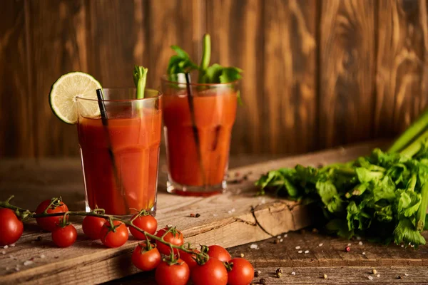Bloody mary cocktail in glasses on wooden background with salt, pepper, tomatoes and celery — Stock Photo